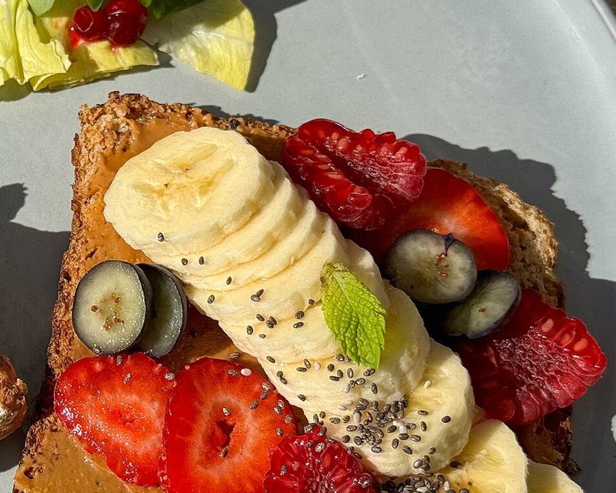 Toast spread with nut butter and topped with banana slices, strawberries and blueberries