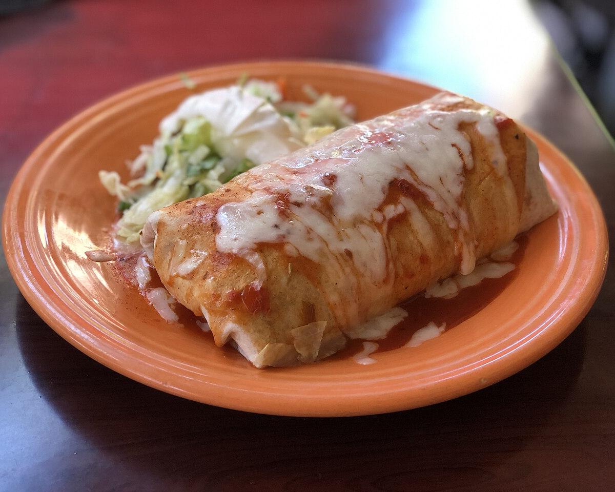 A burrito topped with melted cheese on an orange plate