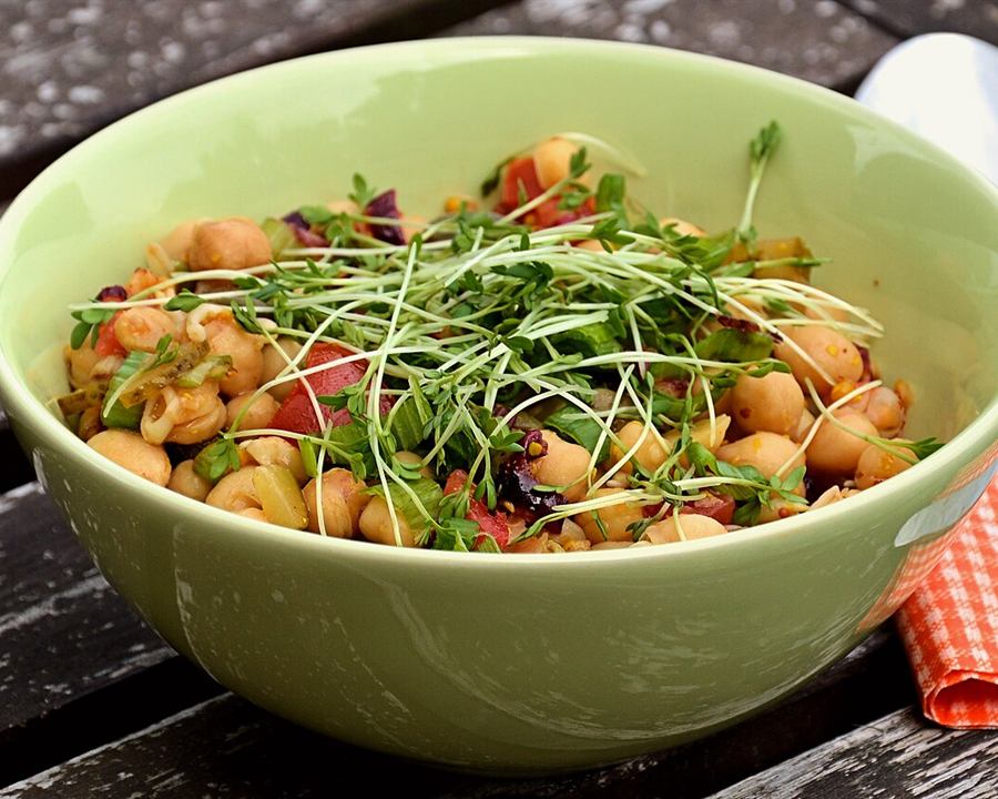 A green bowl of chickpea salad with cherry tomatoes and garden cress