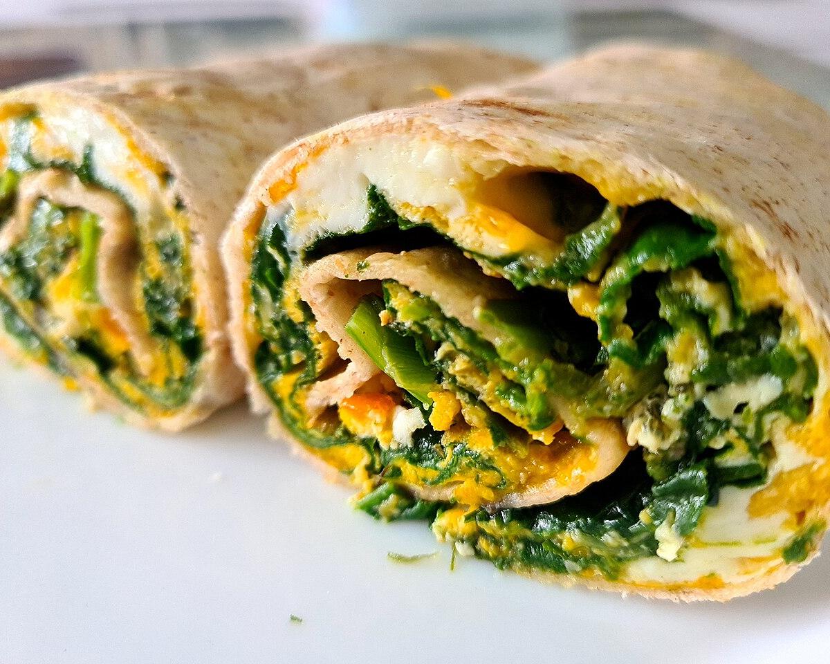 A tortilla wrap filled with spinach and egg, cut in half