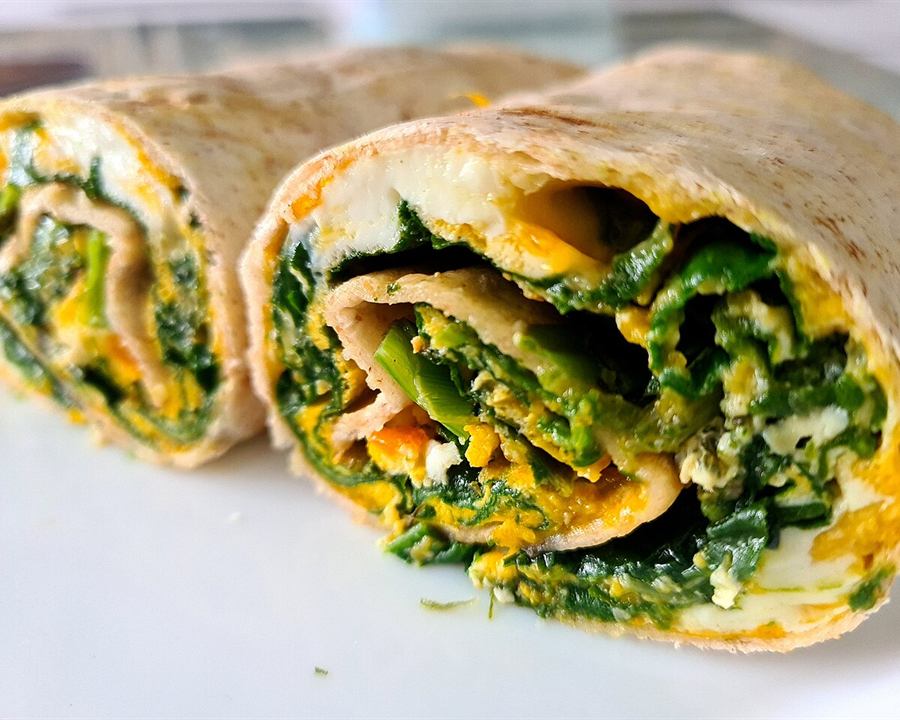 A tortilla wrap filled with spinach and egg, cut in half