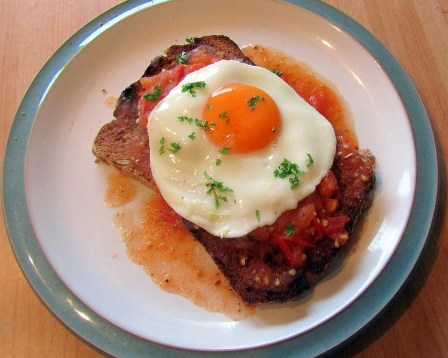 A fried egg on toast with tomato relish and fresh herbs on a plate