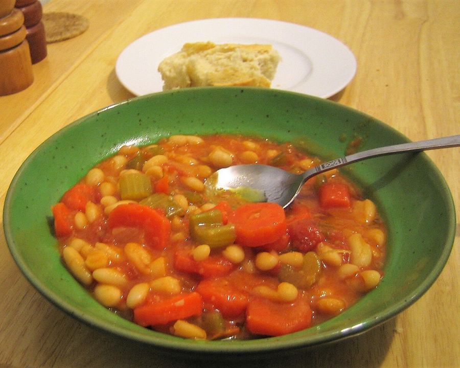 White bean soup with carrots, celery and tomato in a green bowl