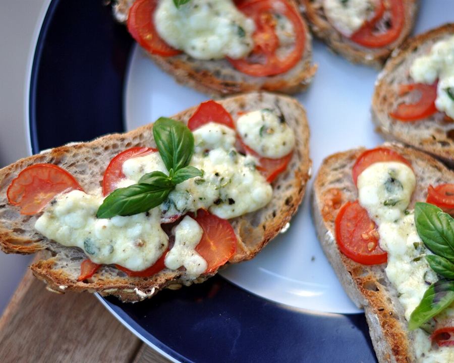 Toasted bread topped with tomato slices, soft white cheese and basil