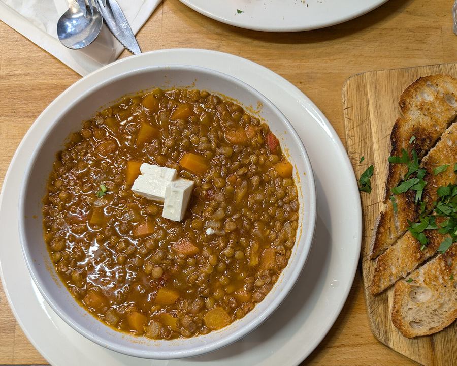 A bowl of lentil soup with a cube of feta, served with toasted bread