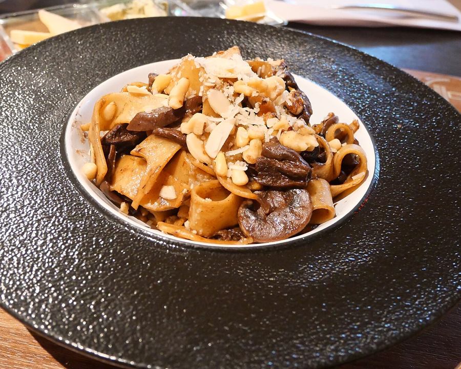 A bowl of pasta with sliced mushrooms and nuts