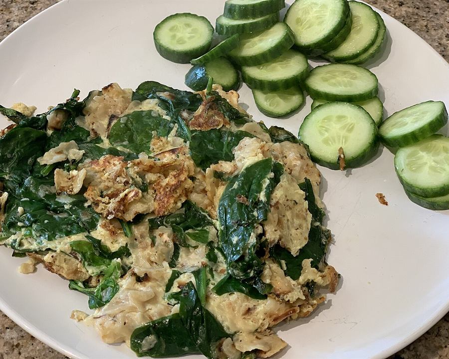 Scrambled eggs with spinach and sliced cucumber on a plate