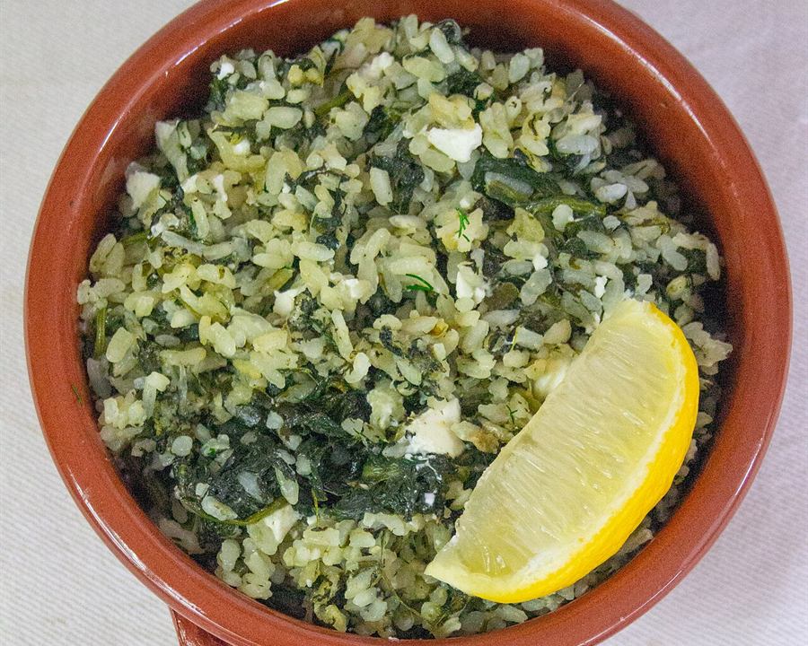 Greek spinach rice (spanakorizo) in a terracotta dish with a lemon wedge