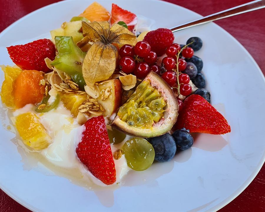 Natural yogurt topped with fresh fruit, honey and granola on a white plate