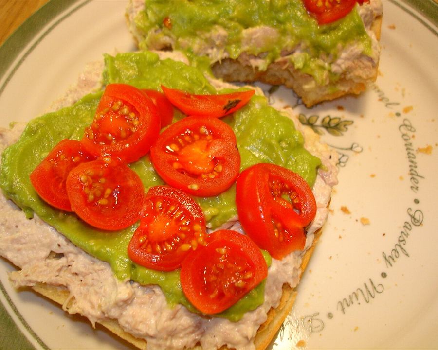 An open-faced tuna sandwich with guacamole and cherry tomatoes