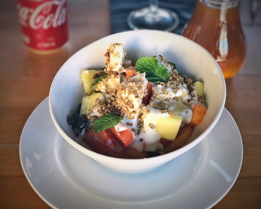 A white bowl of yogurt with pieces of fruit, granola and mint